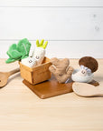 Set of toy vegetables and a wooden spoon on a light wooden surface with a white background