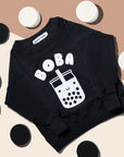 Black sweatshirt with screen printed white ink text BOBA above a smiling glass of boba.