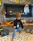 A child modeling a black sweatshirt with screen printed white ink text BOBA above a smiling glass of boba.