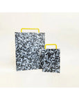 Large and small black and white confetti colored cutting board with a yellow handle on side.