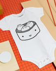 White short sleeved baby bodysuit screen printed with smiling bamboo steamer with three dumplings inside.