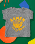 Grey tee screen printed with yellow ink text RAMEN above a smiling bowl of ramen with chopsticks, and soup spoon.