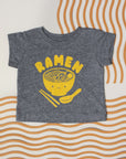 Grey tee screen printed with yellow ink text RAMEN above a smiling bowl of ramen with chopsticks, and soup spoon.