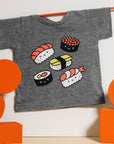 Grey tee screen printed with five pieces of sushi colored white, black, red, and yellow.