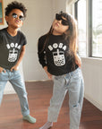 Children modeling black sweatshirts with screen printed white ink text BOBA above a smiling glass of boba.