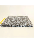 Black and white confetti colored cutting board with a yellow handle on side.