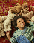 A child lying with four baby dolls wearing bunny costumes in various skin tones.