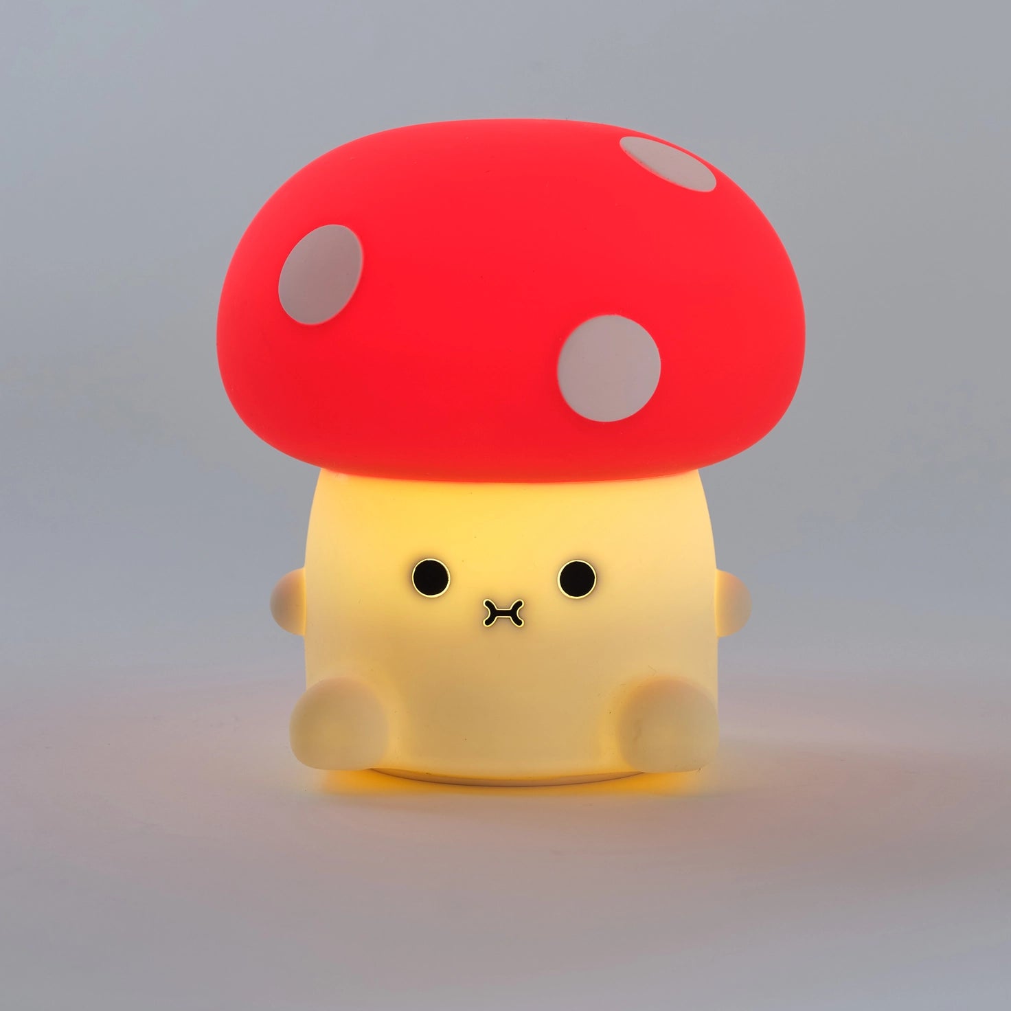 Mushroom shaped night light lit up and  glowing with cute face and red cap and white spots.