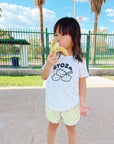 A child modeling a white tee with screen printed black ink text GYOZA above three smiling dumplings.