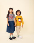 A child modeling a grey tee screen printed with red ink text LUMPIA above three smiling lumpia and dipping sauce. Another child modeling a yellow sweater with a screen printed red bowl with white rice and the text RICe above in black.