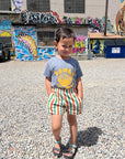 A child modeling a grey tee screen printed with yellow ink text RAMEN above a smiling bowl of ramen with chopsticks, and soup spoon.