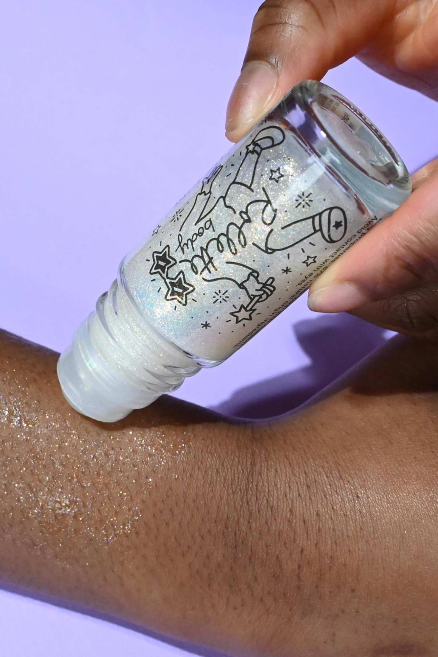 Hand holding a bottle of glittery product applied to skin against a purple background