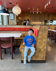 A child modeling a blue sweatshirt screen printed with orange ink text RAMEN above a bowl of ramen with a smiley face, chopsticks, and soup spoon.