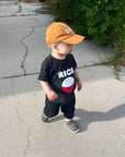 A child modeling a black tee screen printed with white ink text RICE above a red smiling bowl full of white rice.