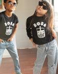 Children modeling black tees with screen printed white ink text BOBA above a smiling glass of boba.