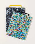 Two cutting boards one black and white confetti with a yellow handle the other red blue yellow and white confetti with a black handle.