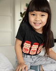 A child modeling a black tee screen printed with three red and yellow yakult yogurt bottles with smiley faces.