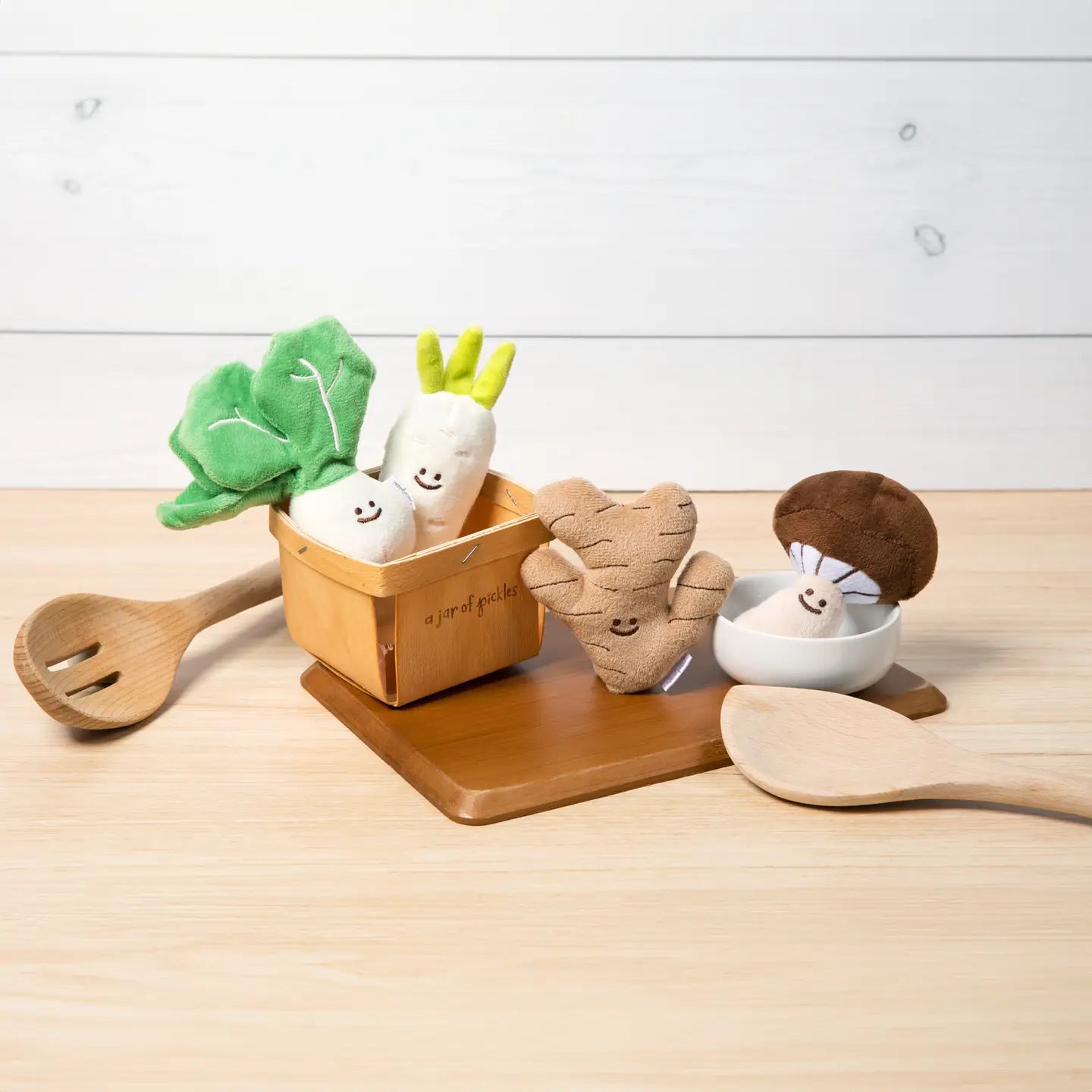 Set of toy vegetables and a wooden spoon on a light wooden surface with a white background