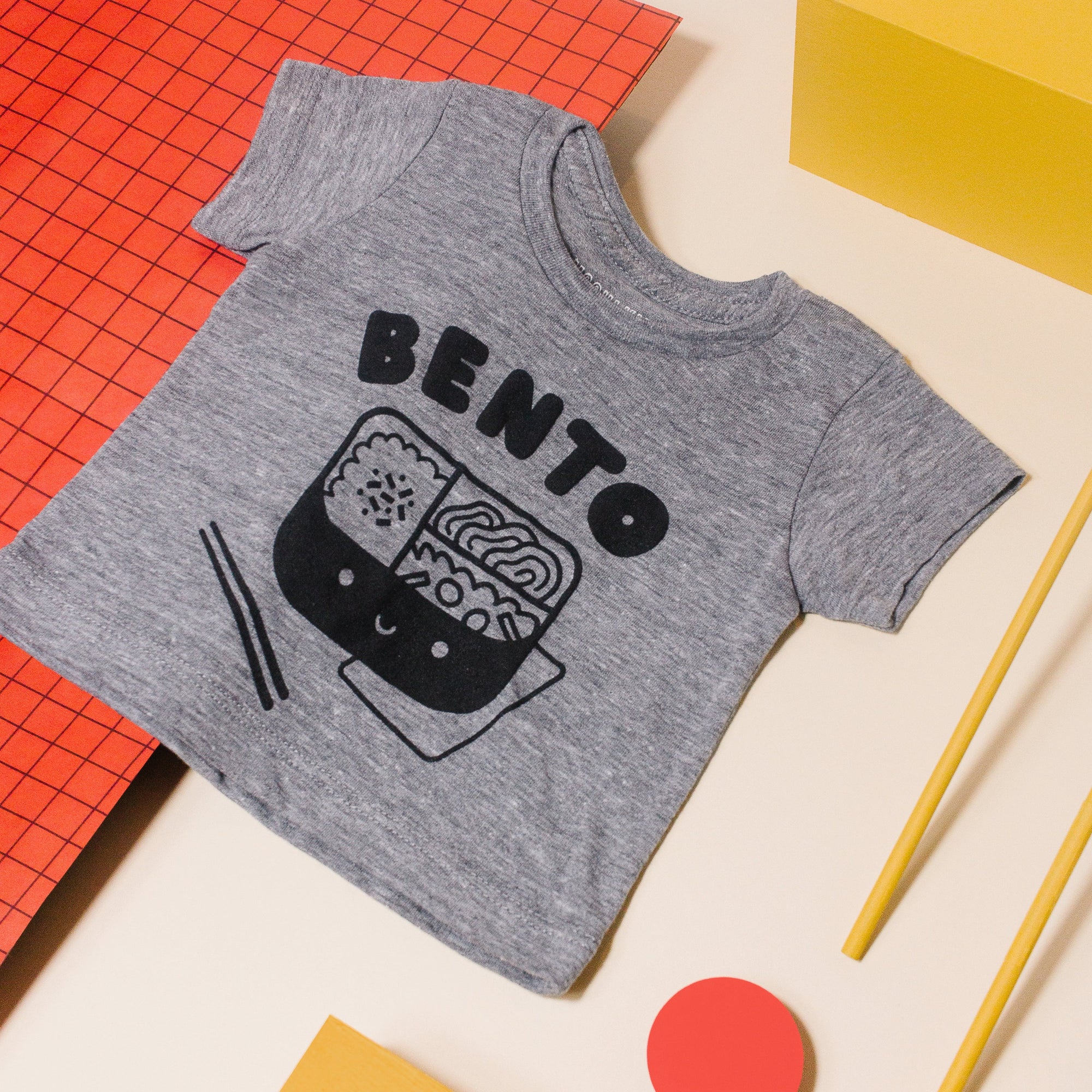 Grey tee screen printed with black ink text BENTO above a black smiling bento box lunch with chopsticks.