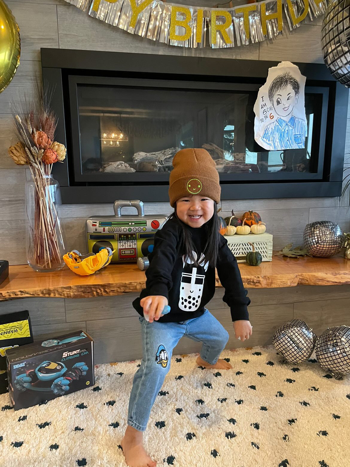 A child modeling a black sweatshirt with screen printed white ink text BOBA above a smiling glass of boba.