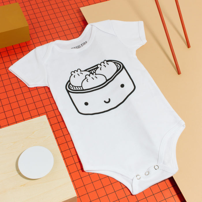 White short sleeved baby bodysuit screen printed with smiling bamboo steamer with three dumplings inside.