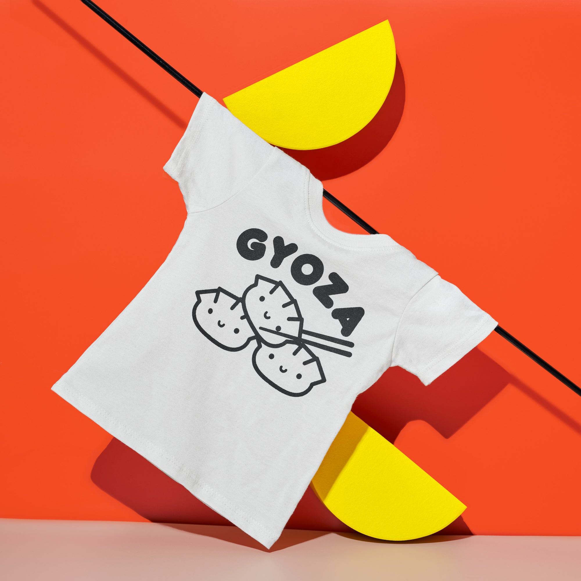 White tee with screen printed black ink text GYOZA above three smiling dumplings.