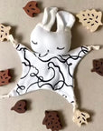 Baby comfort blanket with bunny face surrounded by wooden leaves on a beige background