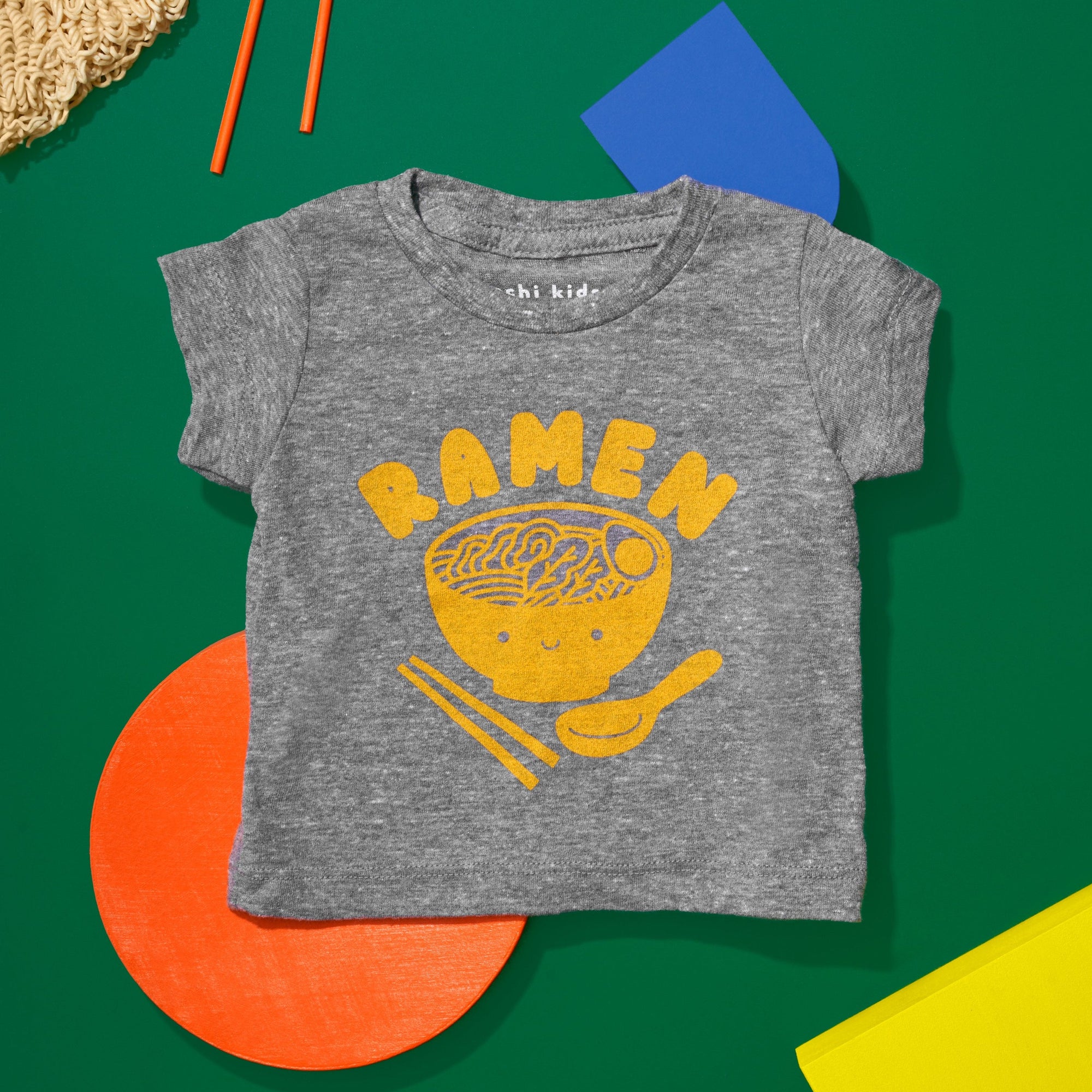 Grey tee screen printed with yellow ink text RAMEN above a smiling bowl of ramen with chopsticks, and soup spoon.