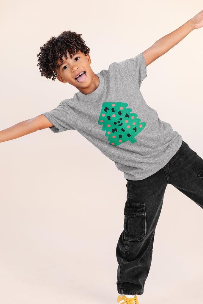 A child modeling a grey tee screen printed with a green Christmas tree with red ornaments, black happy face and MERRY MERRY adorning the tree.