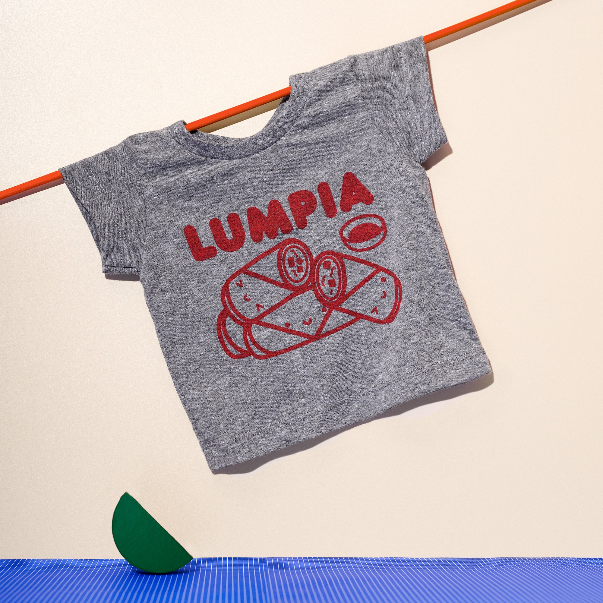 Grey tee screen printed with red ink text LUMPIA above three  smiling lumpia and dipping sauce.