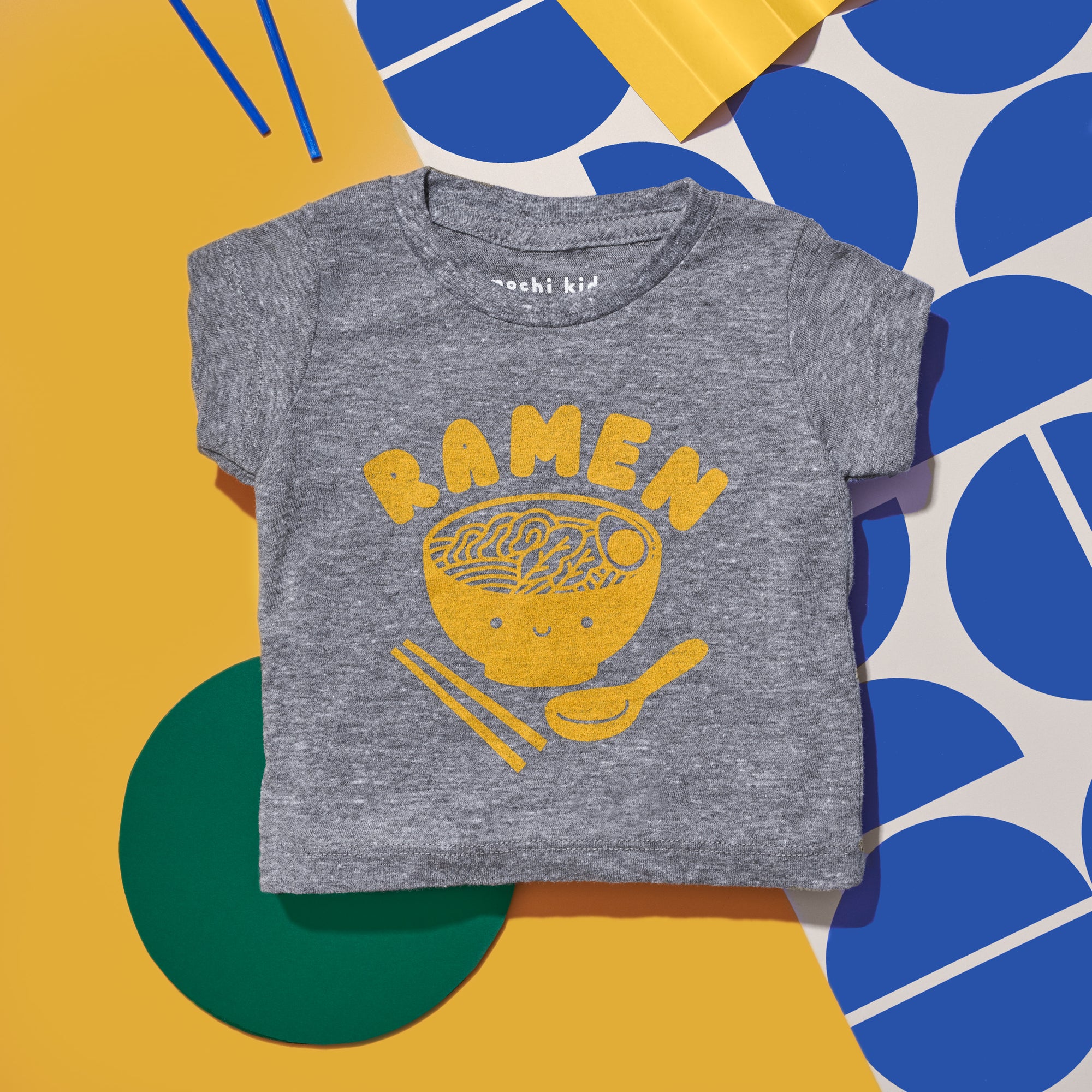 Grey tee screen printed with yellow ink text RAMEN above a smiling bowl of ramen with chopsticks, and soup spoon.