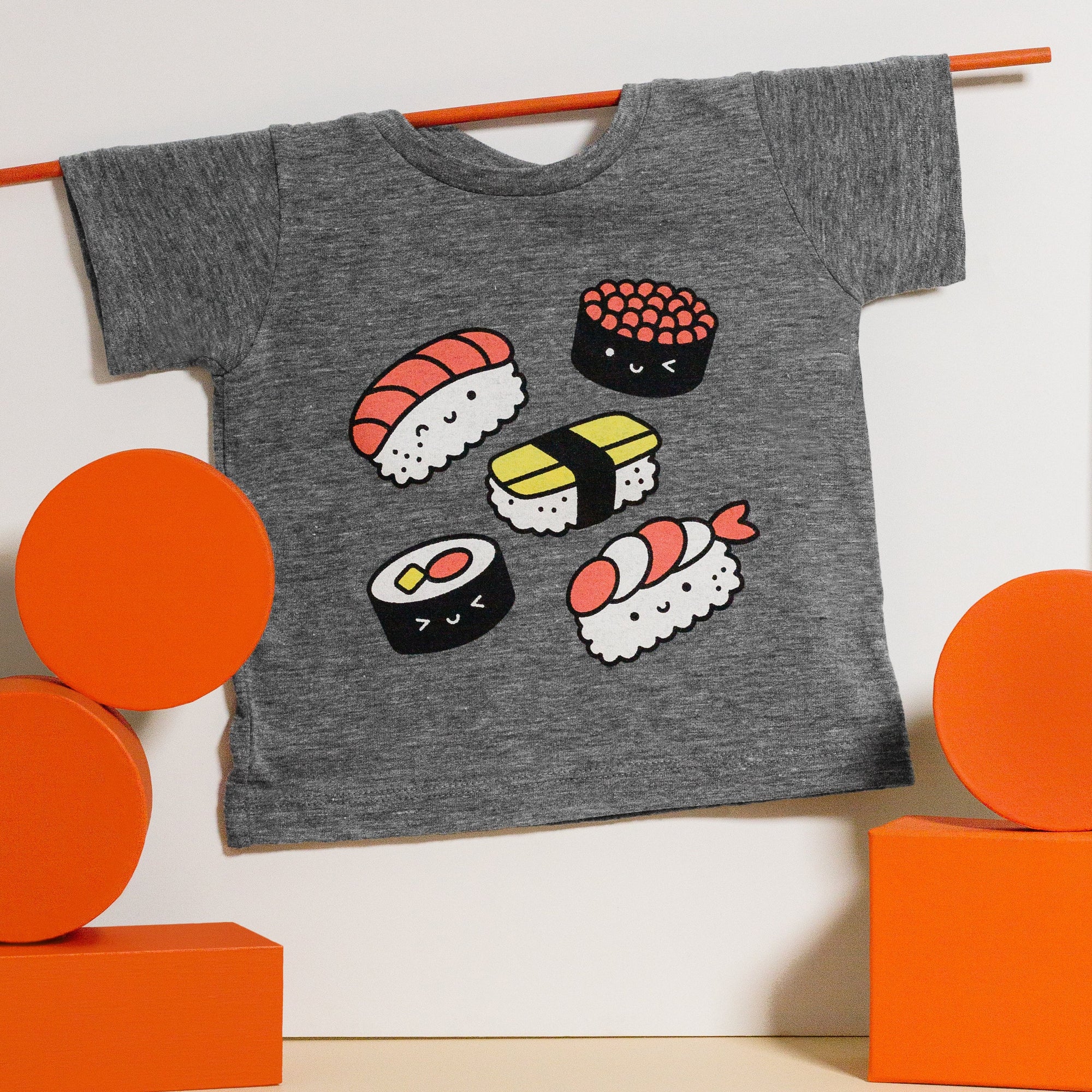 Grey tee screen printed with five pieces of sushi colored white, black, red, and yellow. 
