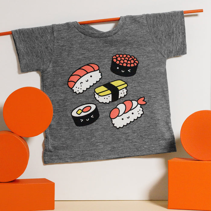 Grey tee screen printed with five pieces of sushi colored white, black, red, and yellow. 