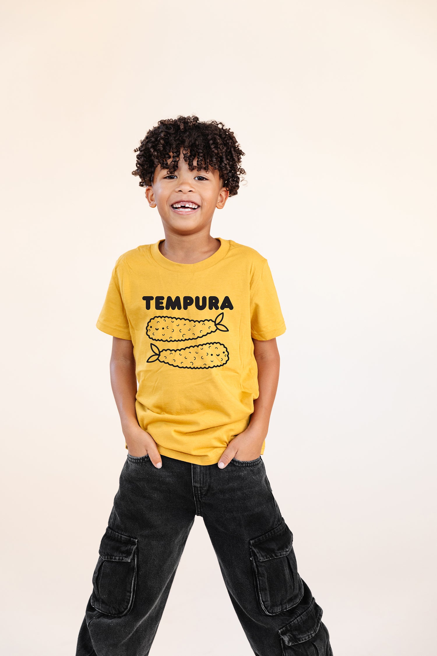 A child modeling a yellow tee with black graphic of word Tempura and two smiling tempura shrimp.