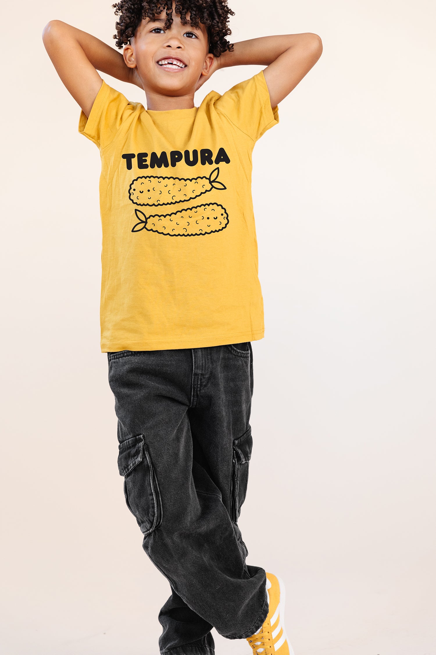 A child modeling a yellow tee with black graphic of word Tempura and two smiling tempura shrimp.