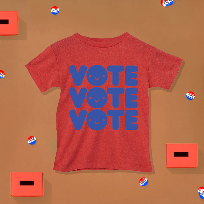 Red tee screen printed with the word "VOTE" three times in blue with a smiley face in the O. 