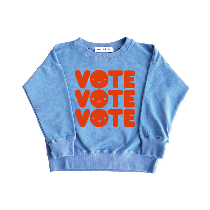 Blue sweatshirt screen printed with the word "VOTE" three times in red with a smiley face in the O