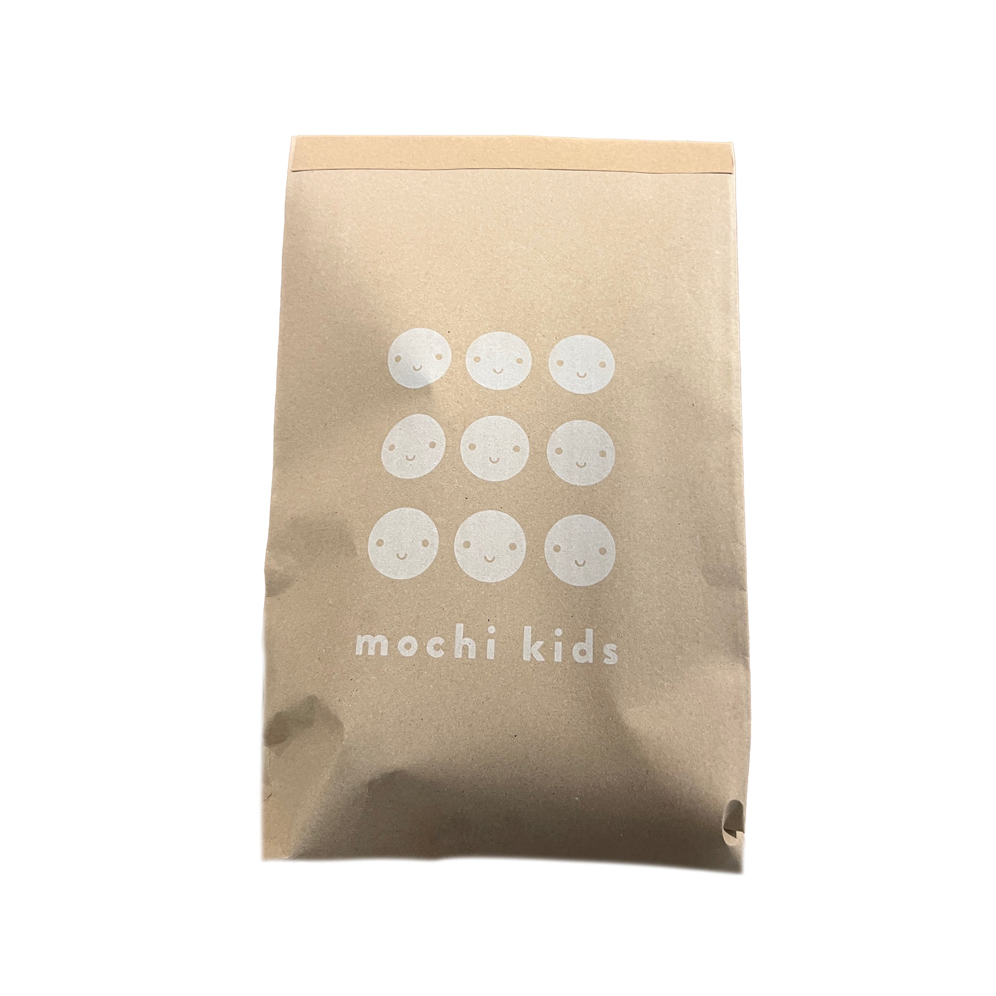 A brown paper blind bag with the Mochi Kids brand name and smiley face graphics printed on it.