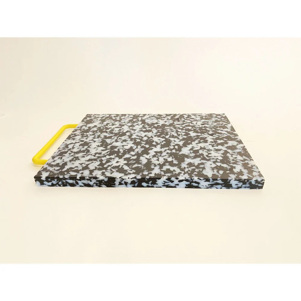 Black and white confetti colored cutting board with a yellow handle on side.