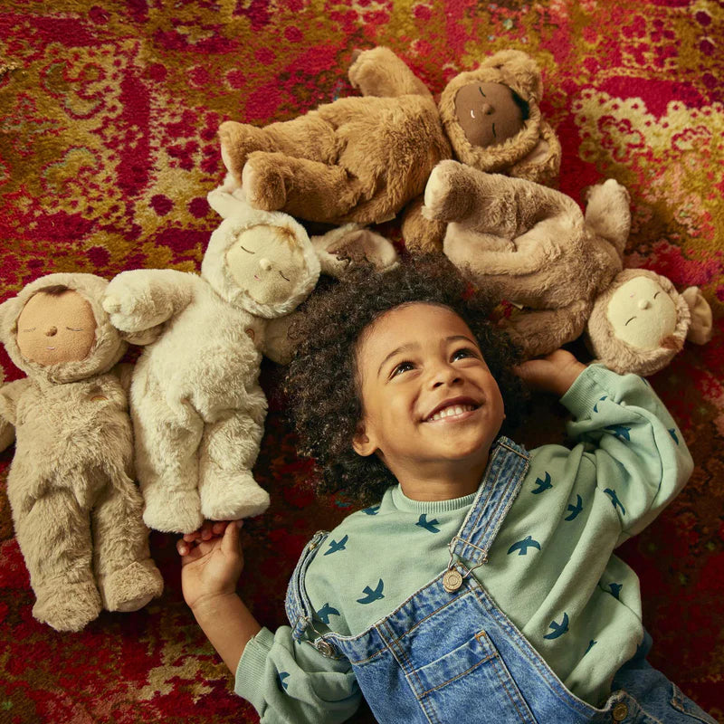 A child lying with four baby dolls wearing bunny costumes in various skin tones.