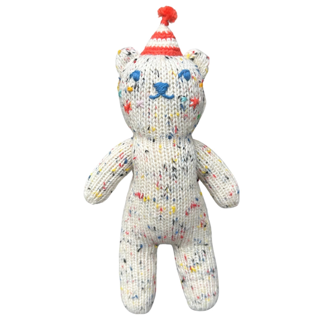 Knitted teddy bear with colorful speckles and a red and white hat on a white background