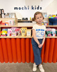 A child modeling a white tee with screen printed with blue ink text DIM SUM and four smiling Dim Sum dumplings.