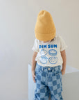 A child modeling a white tee with screen printed with blue ink text DIM SUM and four smiling Dim Sum dumplings.