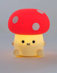 Mushroom shaped night light lit up and  glowing with cute face and red cap and white spots.
