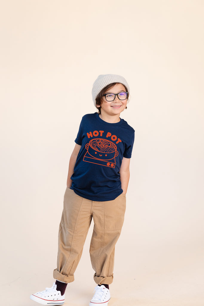 A child modeling a blue tee shirt with red ink screen print of  hot pot bowl on a burner and the text HOT POT.
