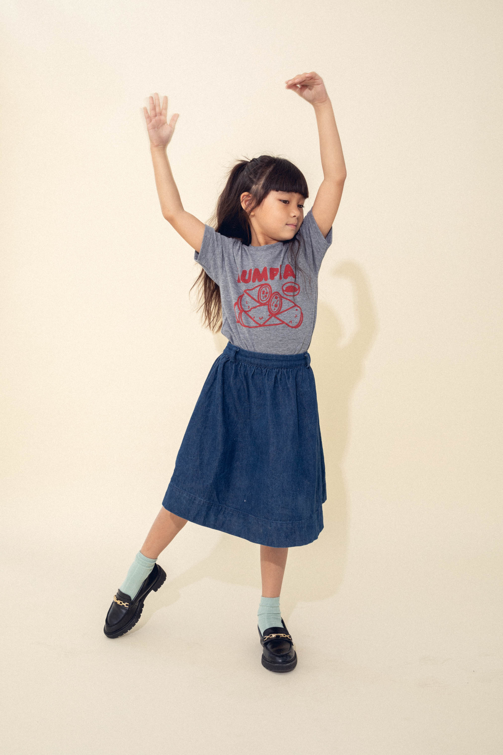 A child modeling a grey tee screen printed with red ink text LUMPIA above three  smiling lumpia and dipping sauce.