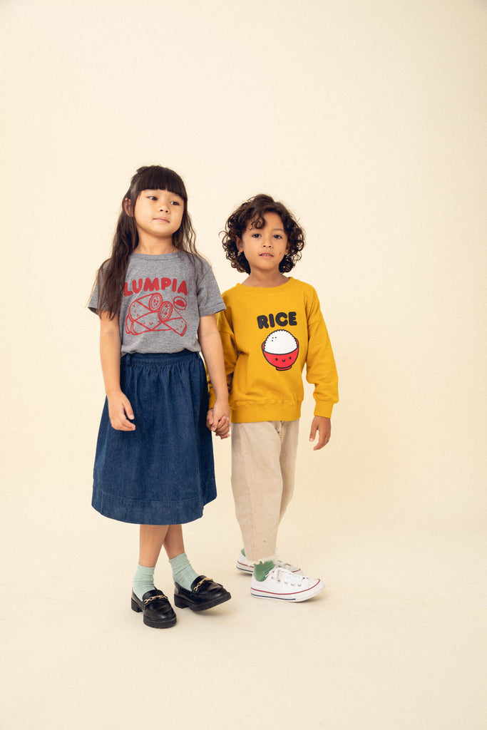 A child modeling a grey tee screen printed with red ink text LUMPIA above three  smiling lumpia and dipping sauce. Another child modeling a yellow sweater with a screen printed red bowl with white rice and the text RICe above in black.