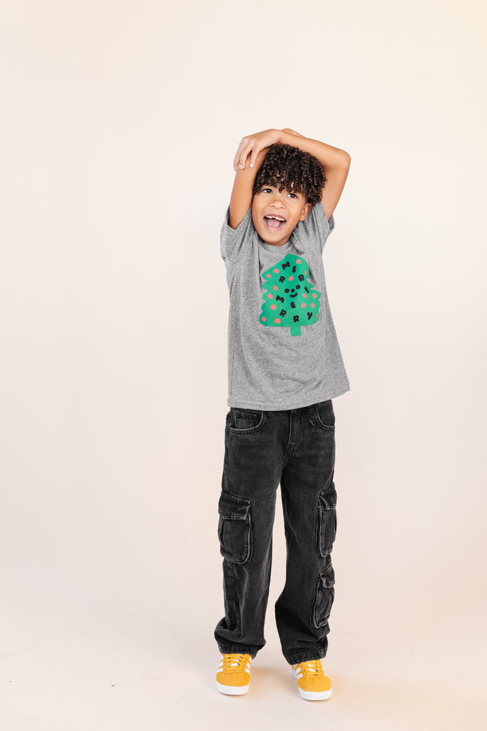A child modeling a grey tee screen printed with a green Christmas tree with red ornaments, black happy face and MERRY MERRY adorning the tree.