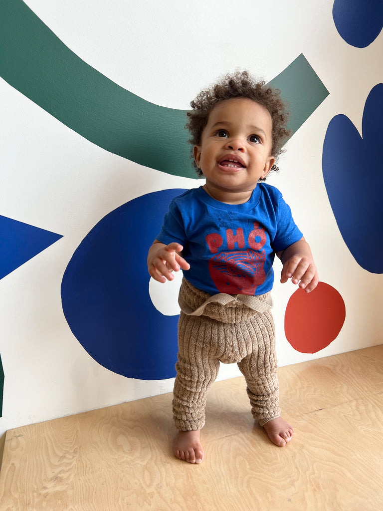 A baby modeling a blue tee screen printed with red ink text Pho above a smiling bowl of Pho.