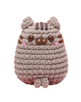 Crocheted plush toy resembling a cat on a pink background, with 'Pusheen' branding.